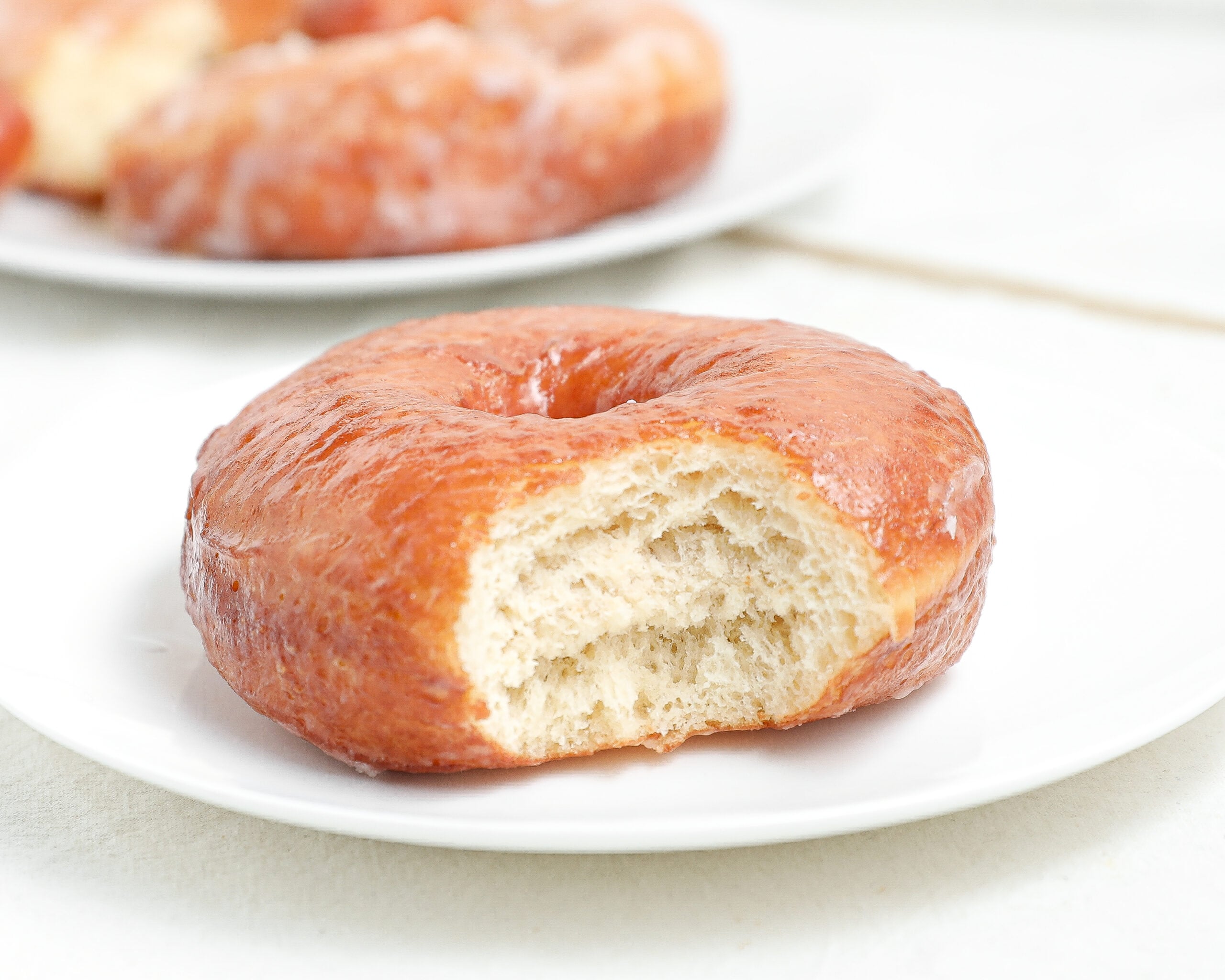 Copycat Krispy Kreme doughnut with vanilla glaze and a bite taken out showing the soft fluffy interior.