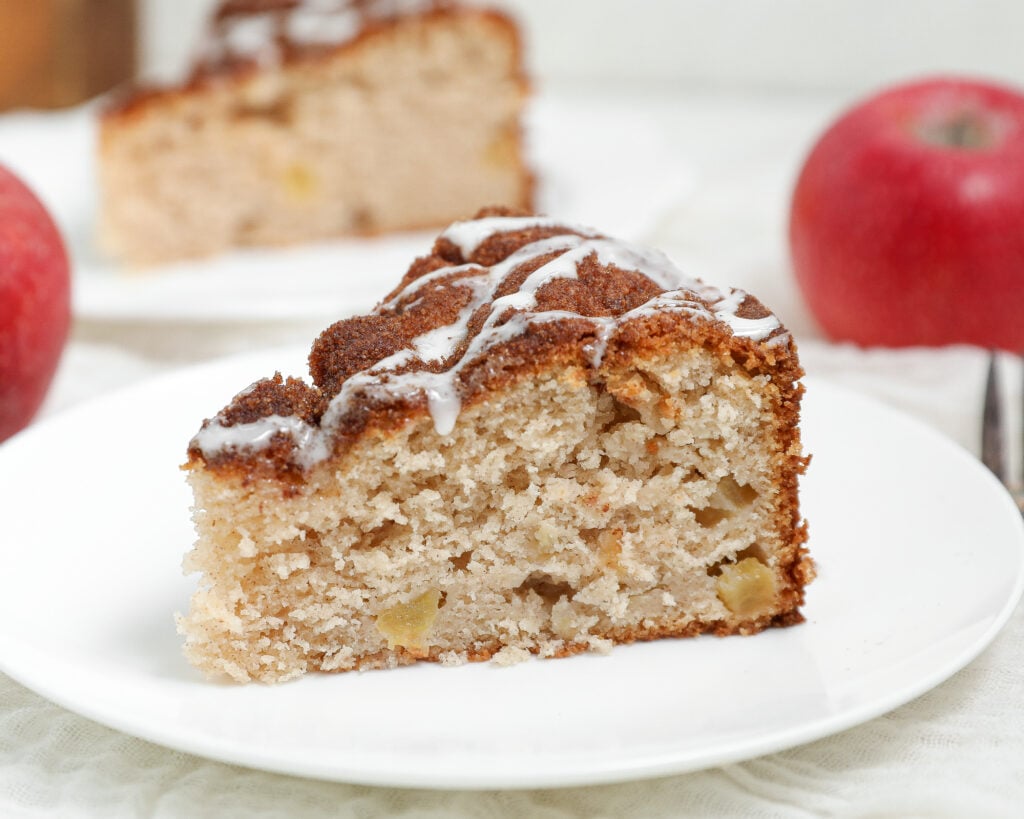 Slice of Apple Cobbler Cake topped with cinnamon sugar and vanilla glaze served on a white plate.