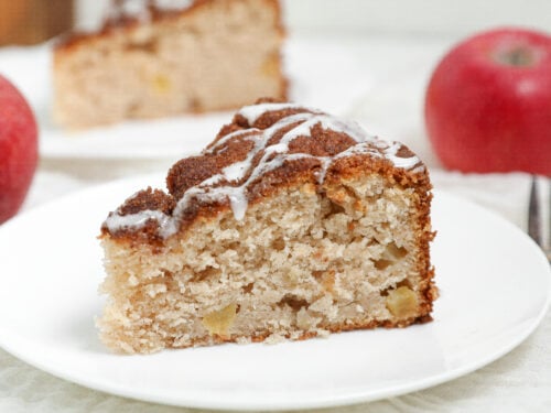 Slice of Apple Cobbler Cake topped with cinnamon sugar and vanilla glaze served on a white plate.