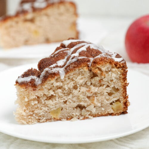 Slice of Apple Cobbler Cake topped with cinnamon sugar and vanilla glaze served on a white plate.