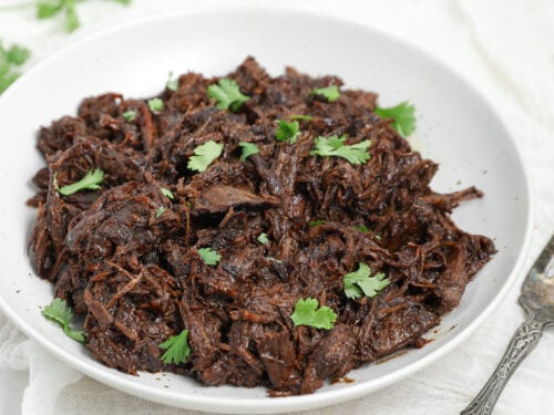 Honey Balsamic Chuck Roast shredded and served in a white bowl with fresh parsley garnish.