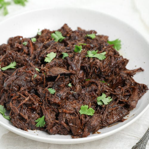 Honey Balsamic Chuck Roast shredded and served in a white bowl with fresh parsley garnish.