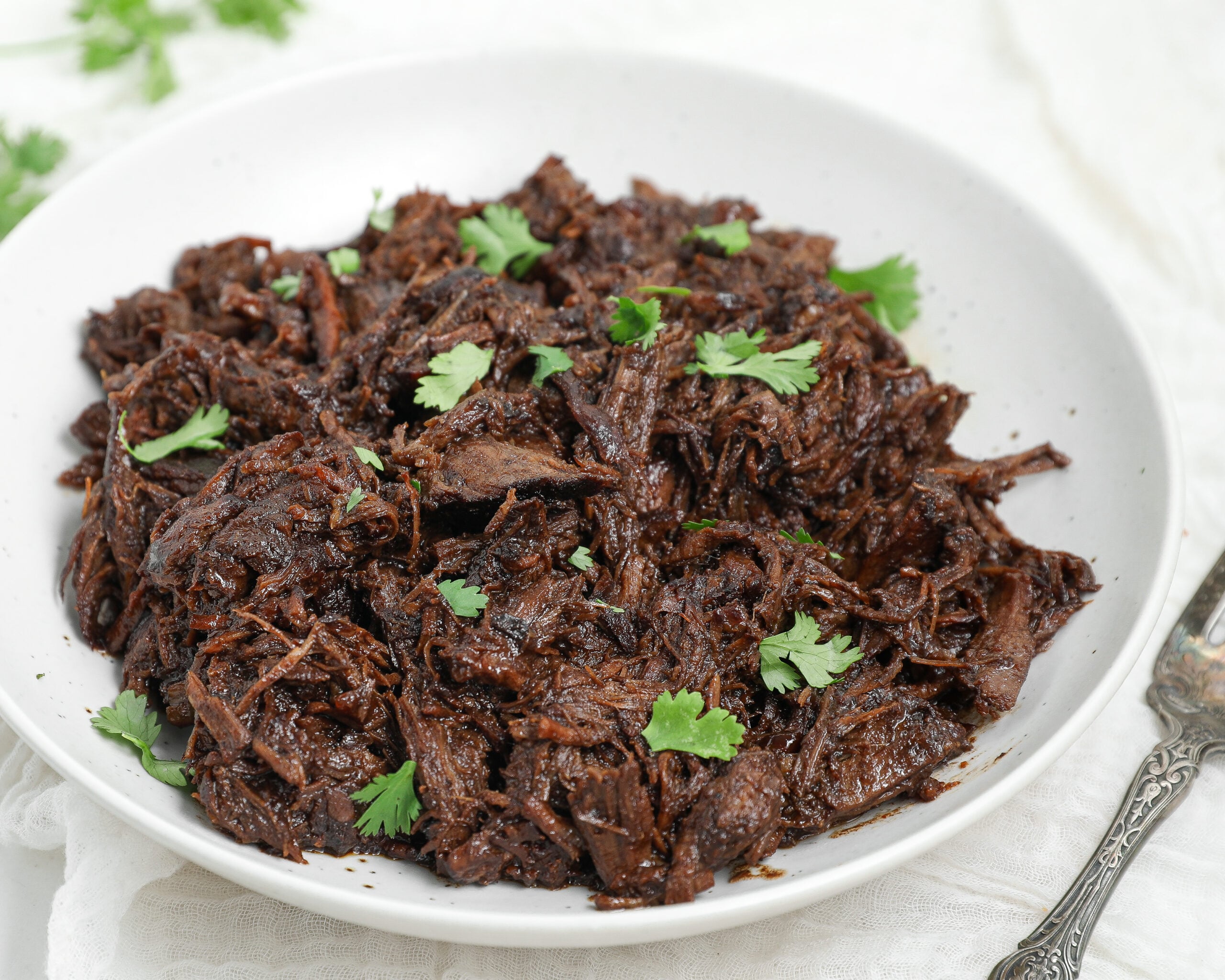 Honey Balsamic Chuck Roast shredded and served in a white bowl with fresh parsley garnish.