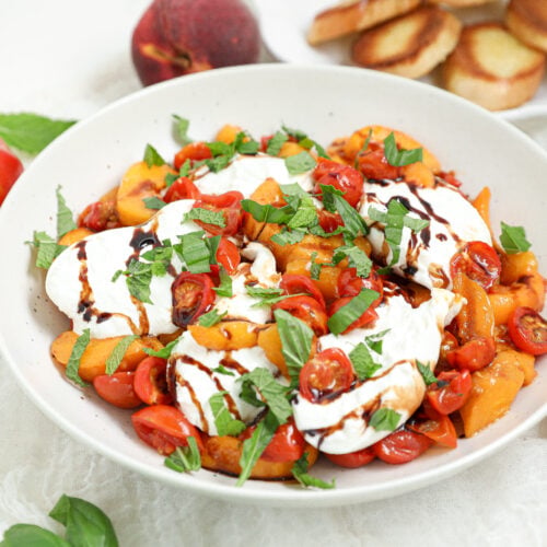 Roasted Tomato Peach Burrata Dip with roasted peaches, cherry tomatoes, creamy burrata, basil, mint, balsamic glaze, and toasted crostini.