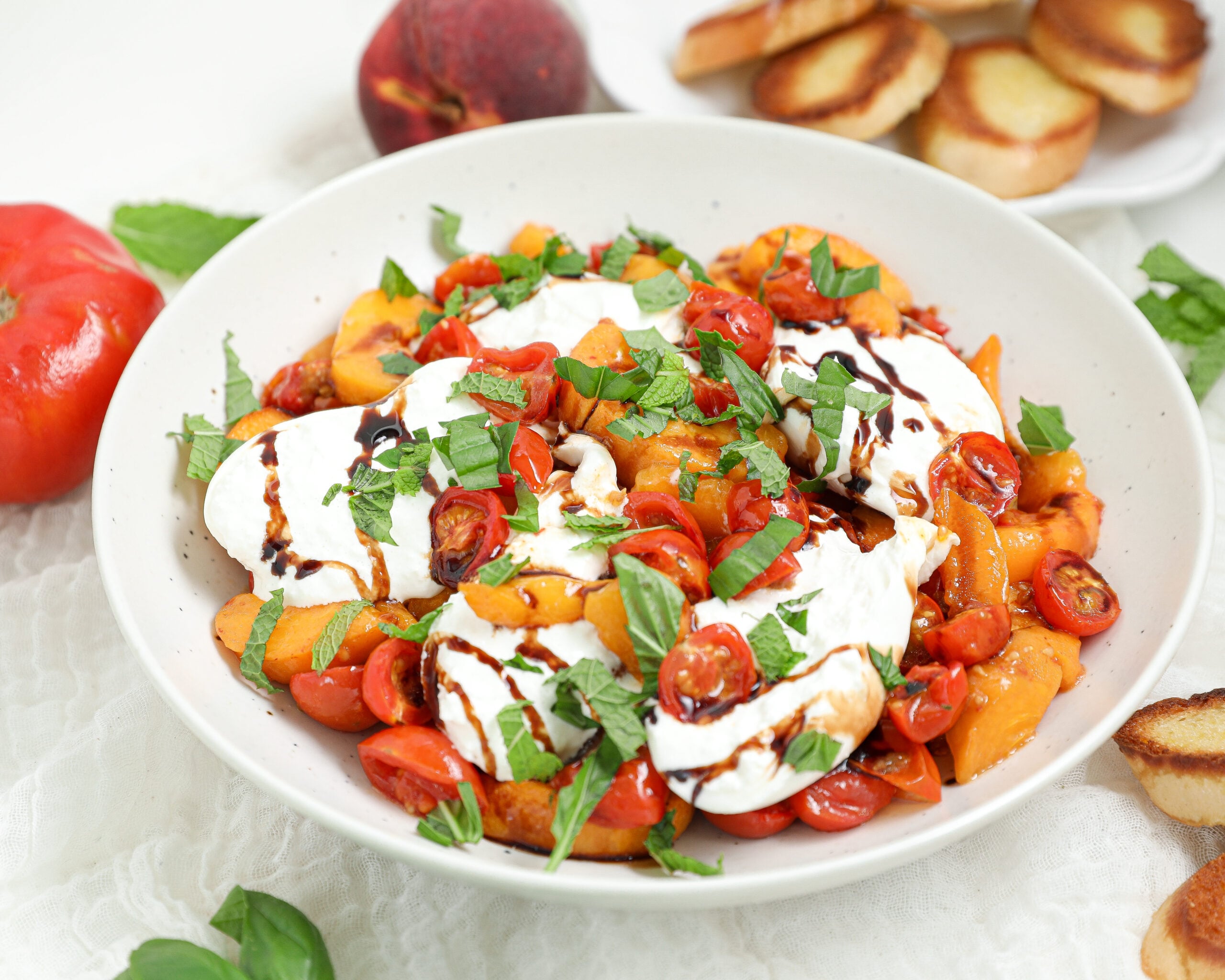 Roasted Tomato Peach Burrata Dip with roasted peaches, cherry tomatoes, creamy burrata, basil, mint, balsamic glaze, and toasted crostini.