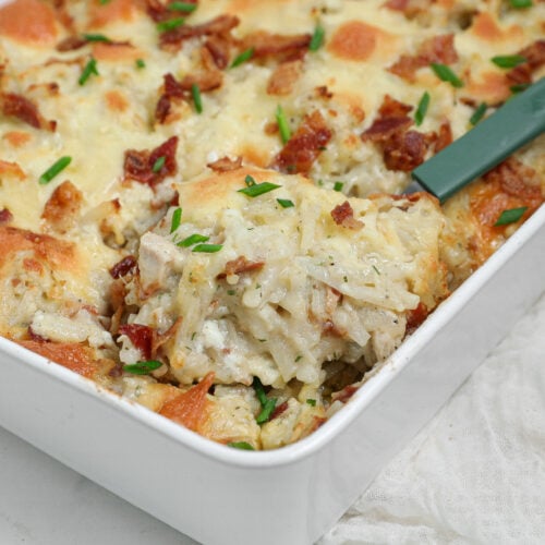 Cheesy Ranch Chicken Hashbrown Casserole with chicken, bacon, melted cheese, shredded potatoes, and fresh chives in a white baking dish.