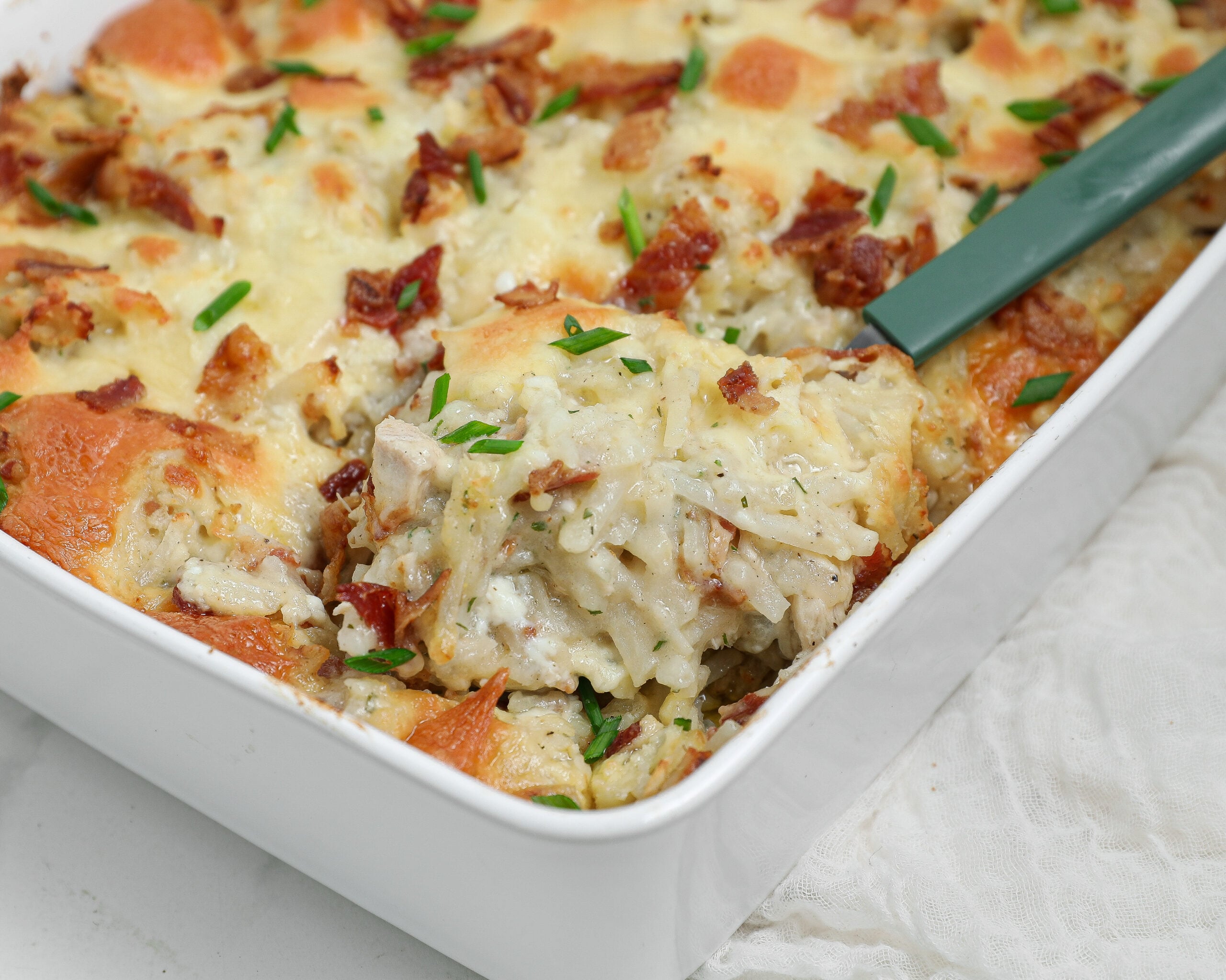 Cheesy Ranch Chicken Hashbrown Casserole with chicken, bacon, melted cheese, shredded potatoes, and fresh chives in a white baking dish.