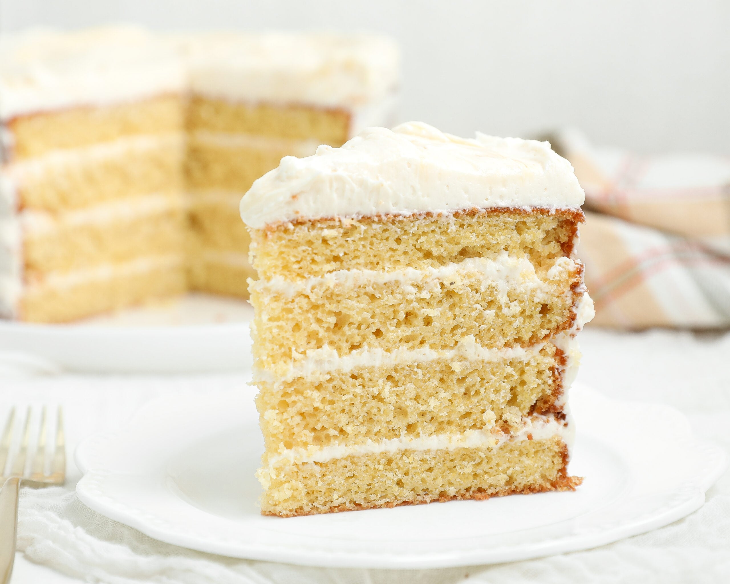 Slice of four-layer Cornbread Cake with Honey Vanilla Frosting on a white plate