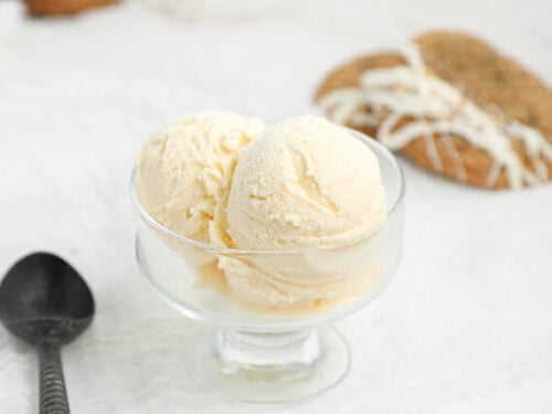 Homemade cream cheese ice cream scoops in a glass dessert bowl with carrot cake cookie ice cream sandwiches in the background