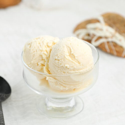 Homemade cream cheese ice cream scoops in a glass dessert bowl with carrot cake cookie ice cream sandwiches in the background
