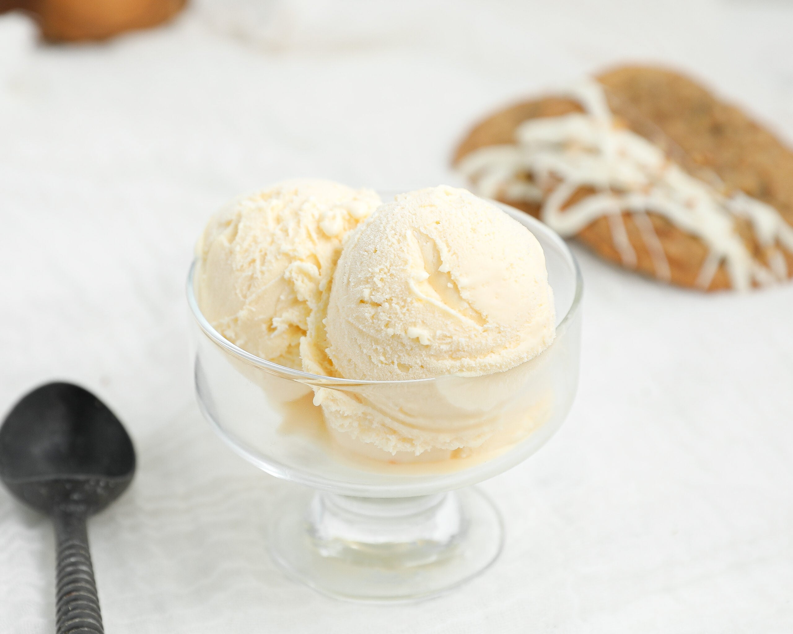 Homemade cream cheese ice cream scoops in a glass dessert bowl with carrot cake cookie ice cream sandwiches in the background