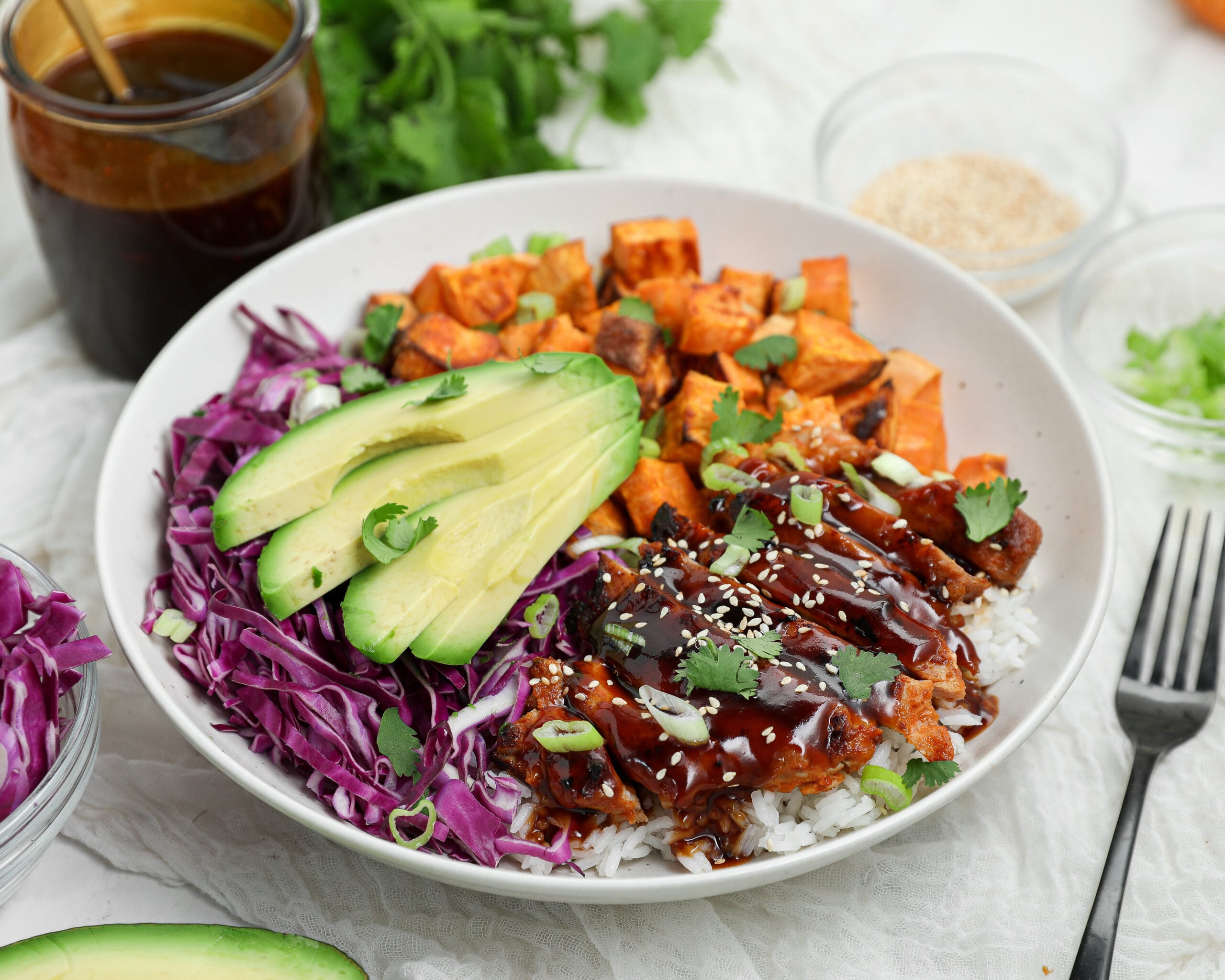 Korean BBQ Chicken Bowl with gochujang chicken, white rice, roasted sweet potatoes, shredded purple cabbage, avocado, and Korean BBQ sauce.