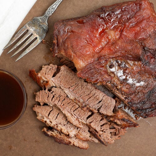 Fork tender oven baked BBQ brisket sliced against the grain with BBQ sauce on the side