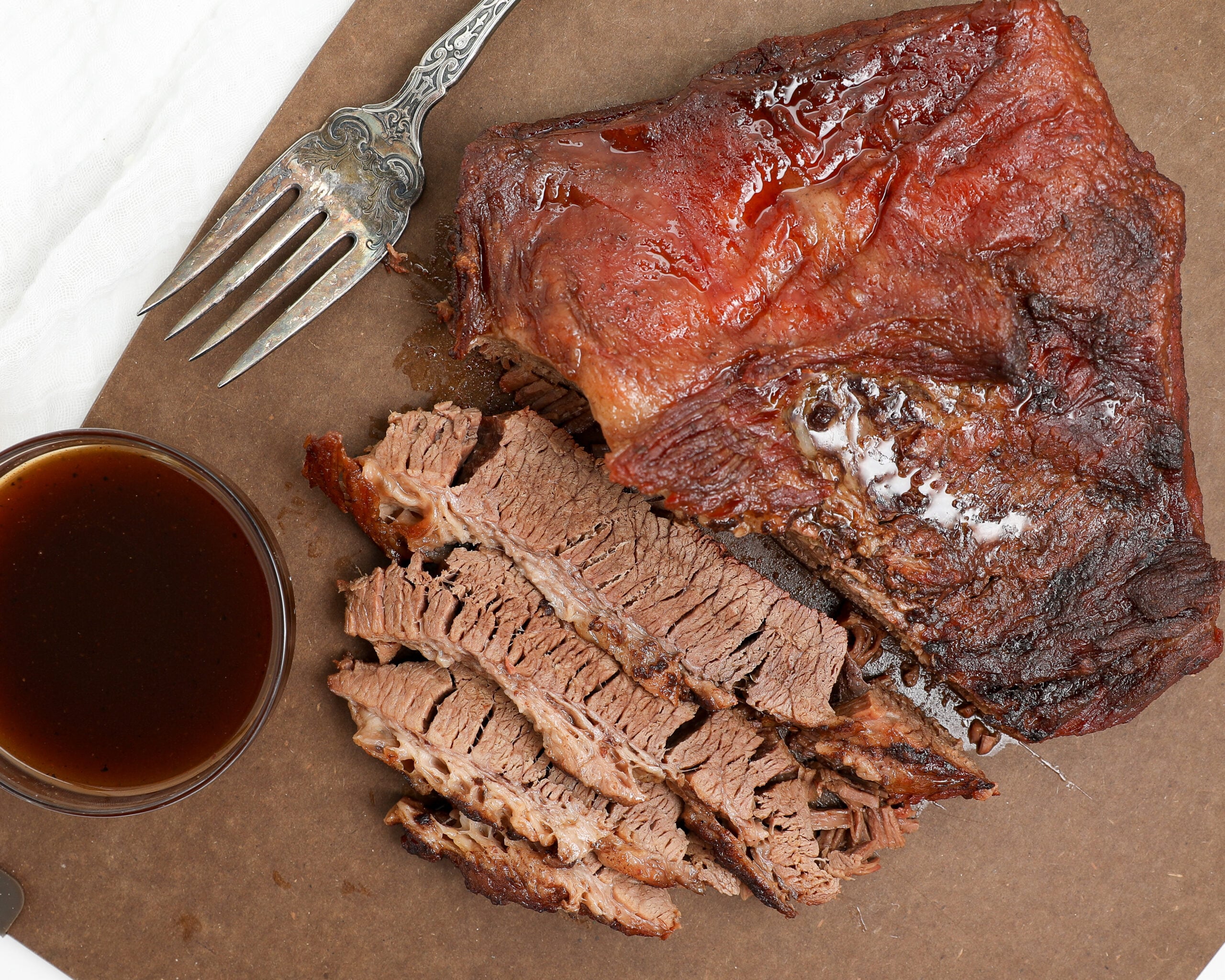 Fork tender oven baked BBQ brisket sliced against the grain with BBQ sauce on the side