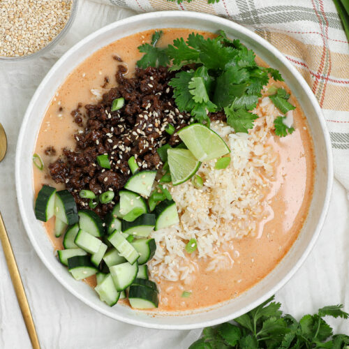 Crispy beef rice broth bowl with coconut curry broth, cucumber, cilantro, lime, and sesame seeds