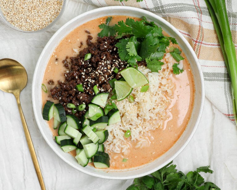Crispy beef rice broth bowl with coconut curry broth, cucumber, cilantro, lime, and sesame seeds