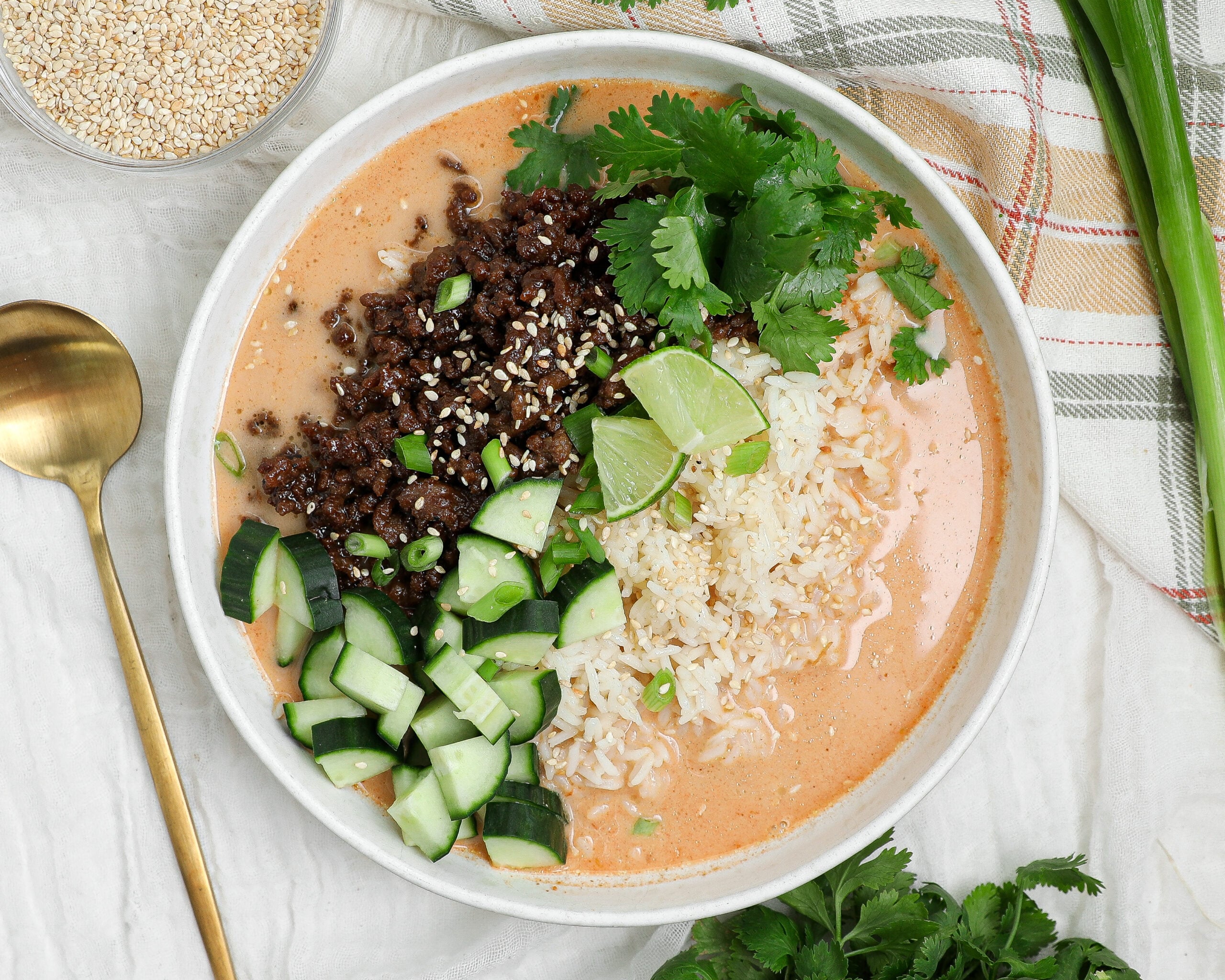 Crispy beef rice broth bowl with coconut curry broth, cucumber, cilantro, lime, and sesame seeds