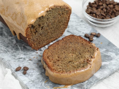 Espresso Banana Bread with a thick coffee glaze, shown as a sliced loaf on a gray marble board with coffee beans in the background.