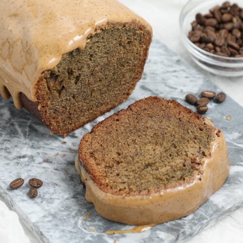Espresso Banana Bread with a thick coffee glaze, shown as a sliced loaf on a gray marble board with coffee beans in the background.