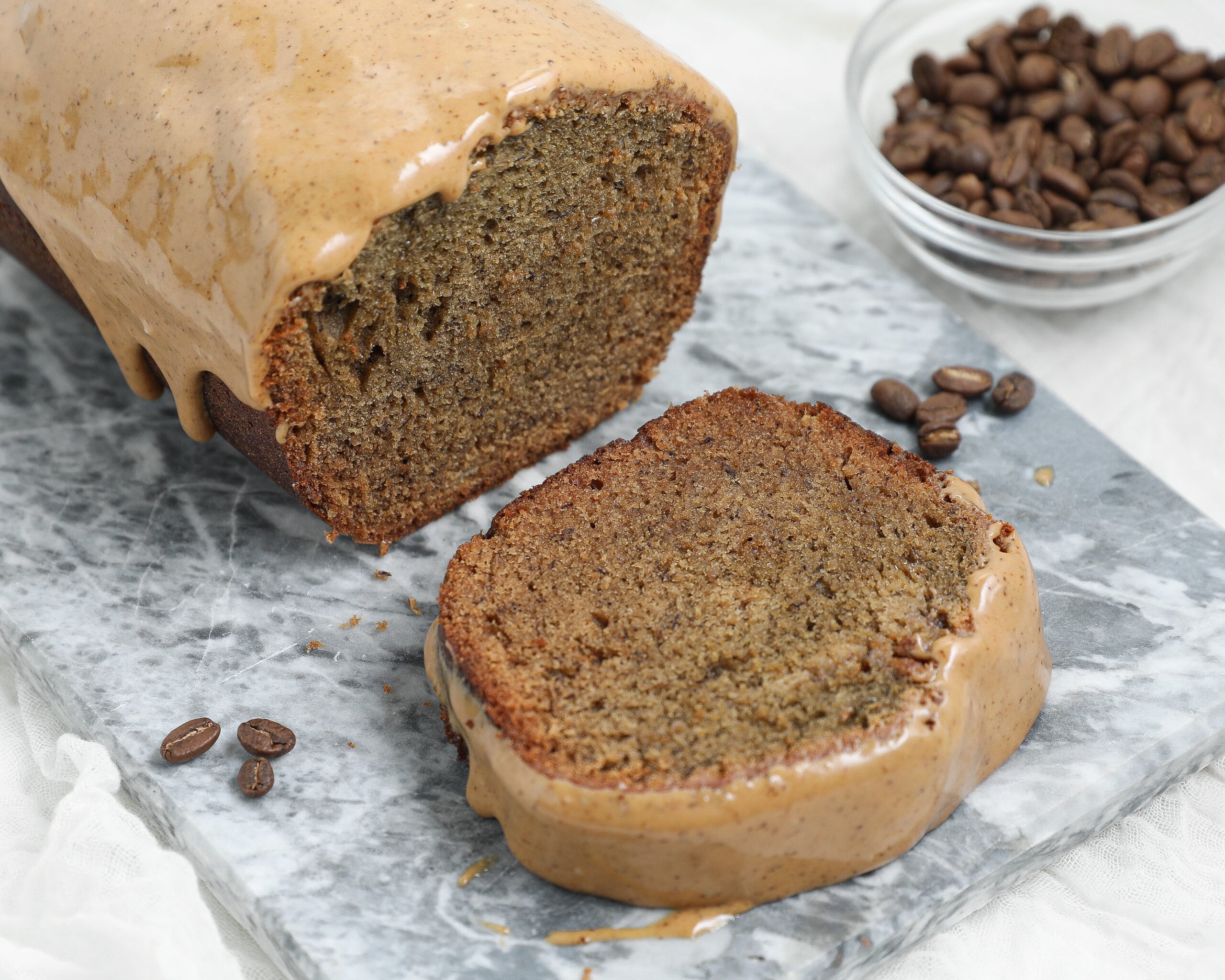 Espresso Banana Bread with a thick coffee glaze, shown as a sliced loaf on a gray marble board with coffee beans in the background.