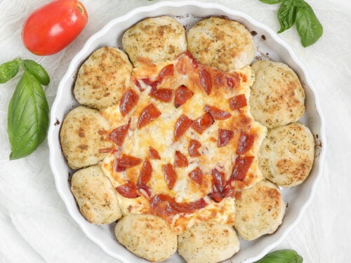 Pizza Dip with Dipping Bread in a white baking dish, with golden pesto-seasoned rolls surrounding melted cheese, pizza sauce, and pepperoni.