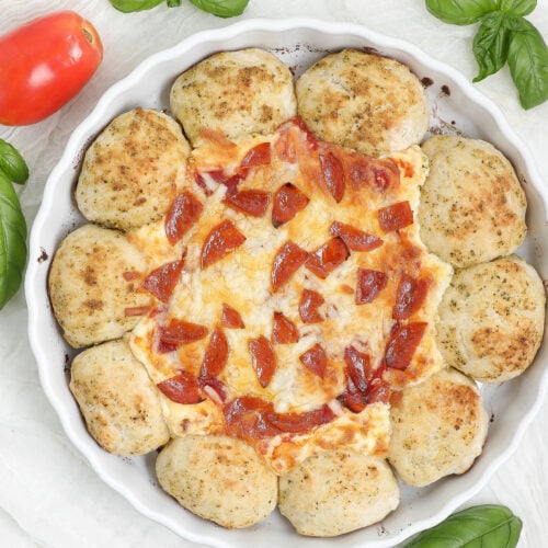 Pizza Dip with Dipping Bread in a white baking dish, with golden pesto-seasoned rolls surrounding melted cheese, pizza sauce, and pepperoni.