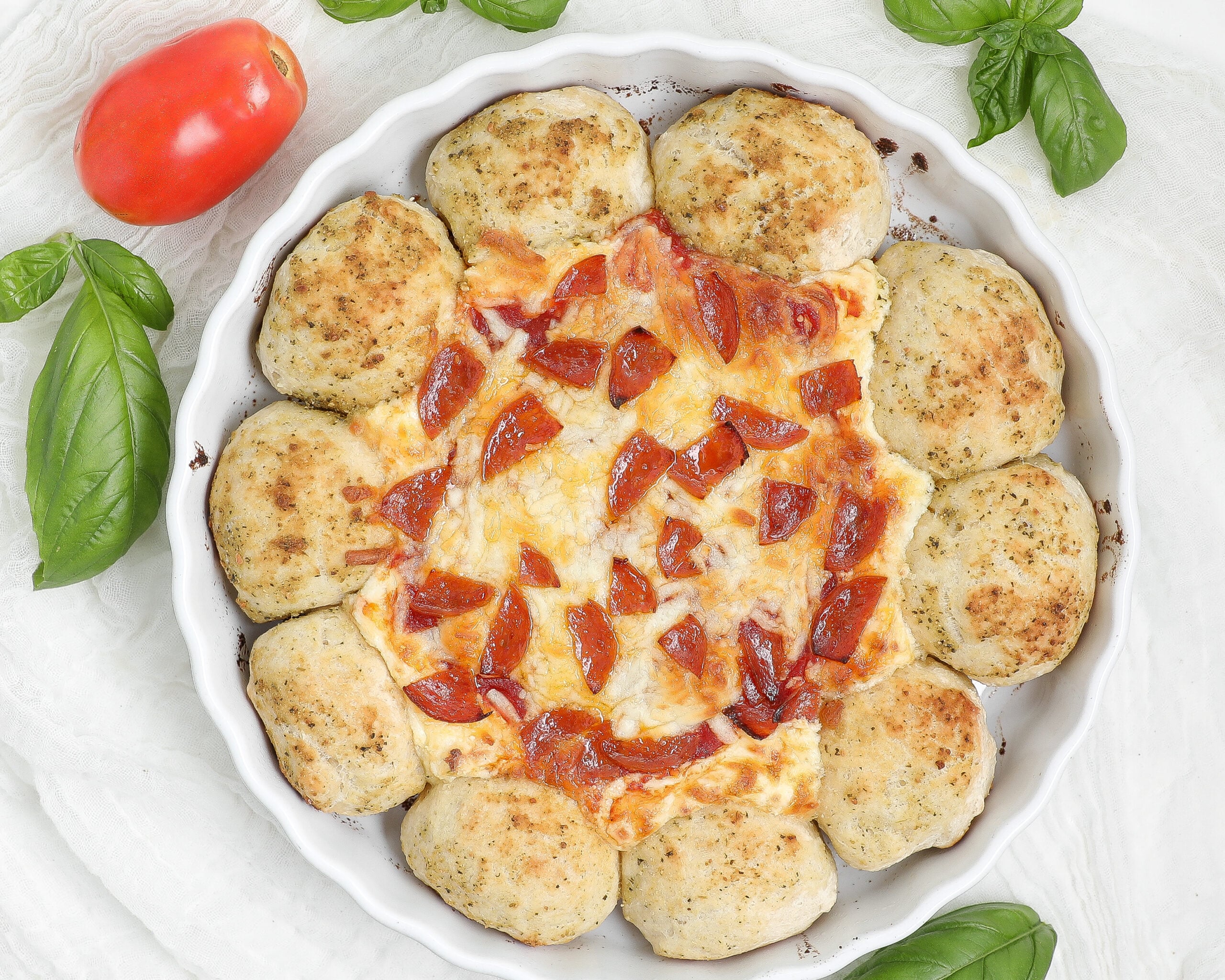 Pizza Dip with Dipping Bread in a white baking dish, with golden pesto-seasoned rolls surrounding melted cheese, pizza sauce, and pepperoni.