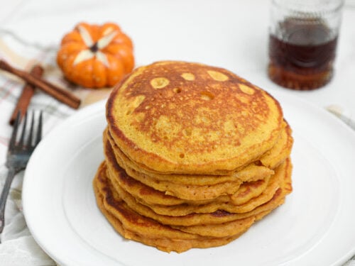 Spiced Pumpkin Cottage Cheese Pancakes stacked on a plate with maple syrup and fall pumpkins.