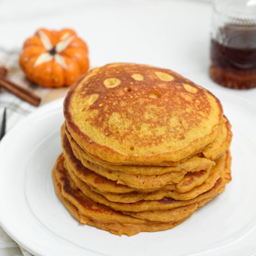 Spiced Pumpkin Cottage Cheese Pancakes stacked on a plate with maple syrup and fall pumpkins.