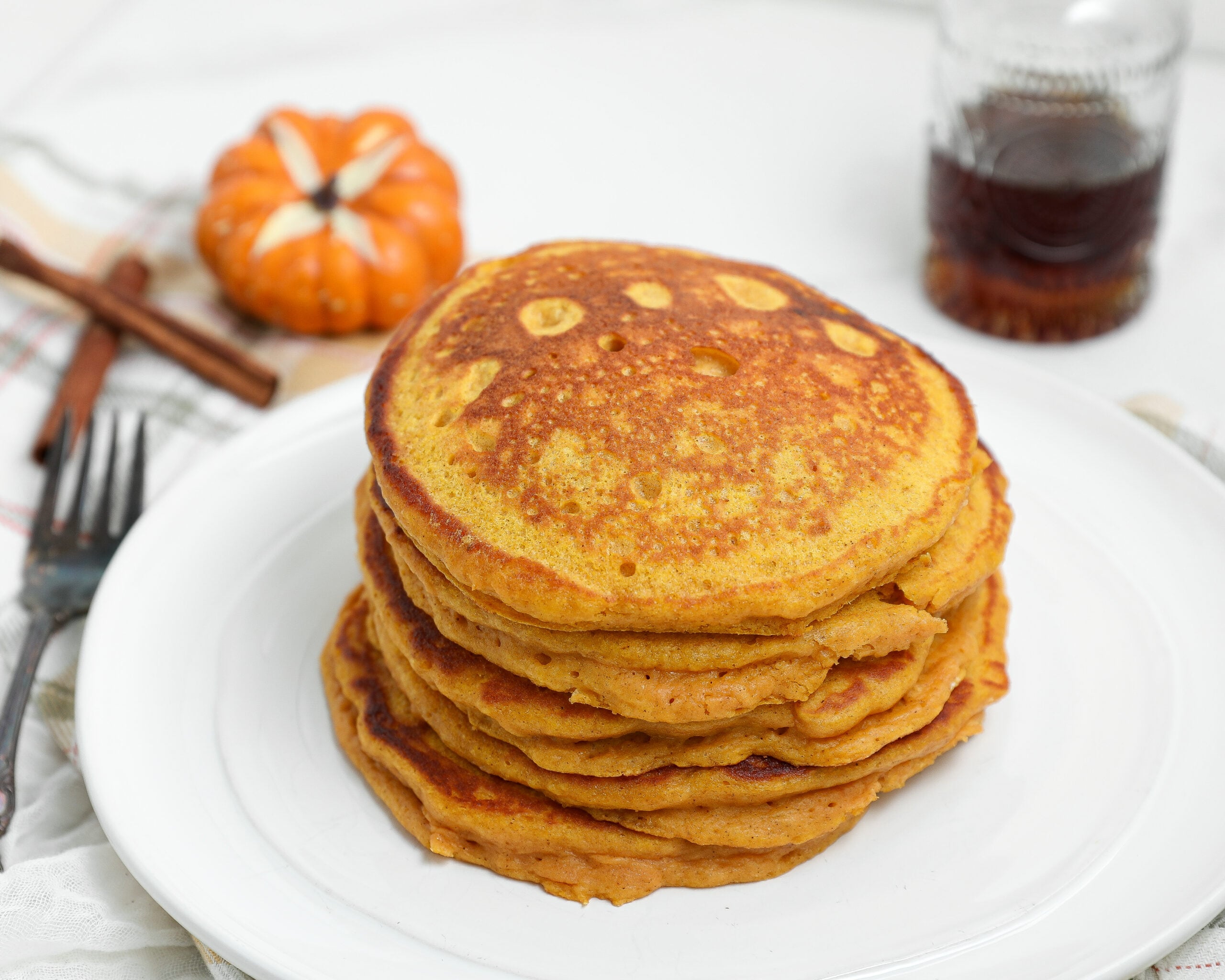Spiced Pumpkin Cottage Cheese Pancakes stacked on a plate with maple syrup and fall pumpkins.