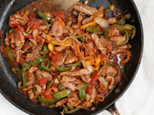 Overhead view of chicken fajitas with tomatoes, bell peppers and onions cooked in a skillet