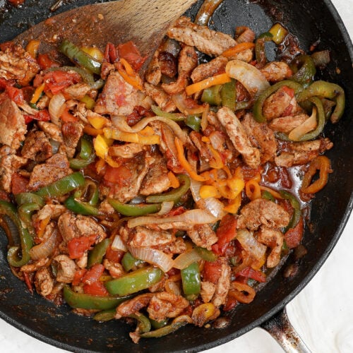 Overhead view of chicken fajitas with tomatoes, bell peppers and onions cooked in a skillet