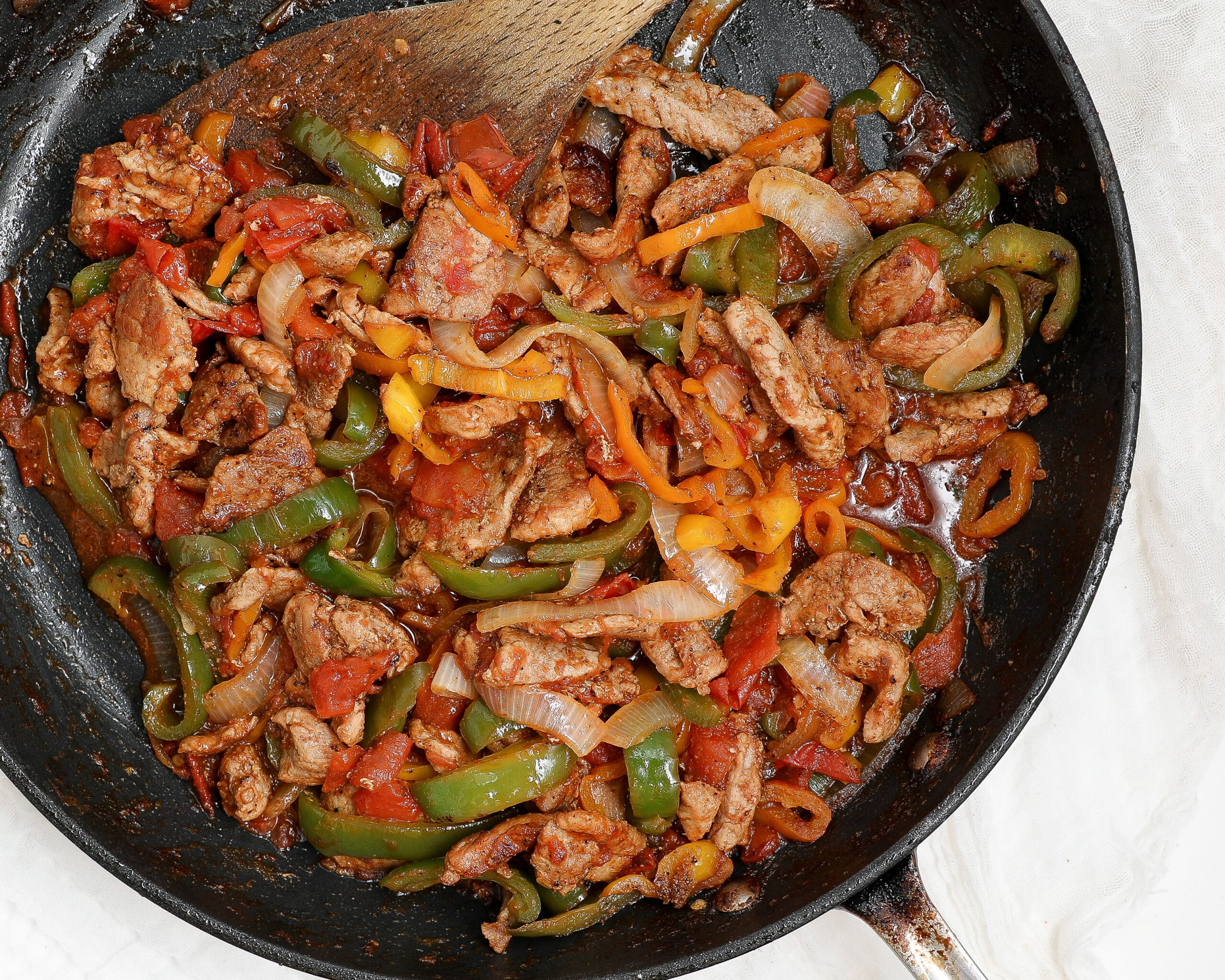 Overhead view of chicken fajitas with tomatoes, bell peppers and onions cooked in a skillet