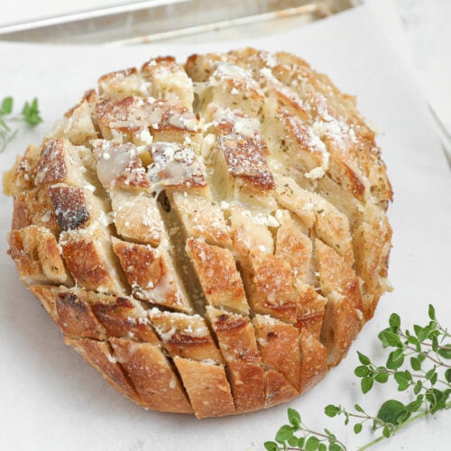 Round loaf of pull apart cheese bread with golden crust, melted mozzarella, Parmesan cheese, and herbs between the slices.
