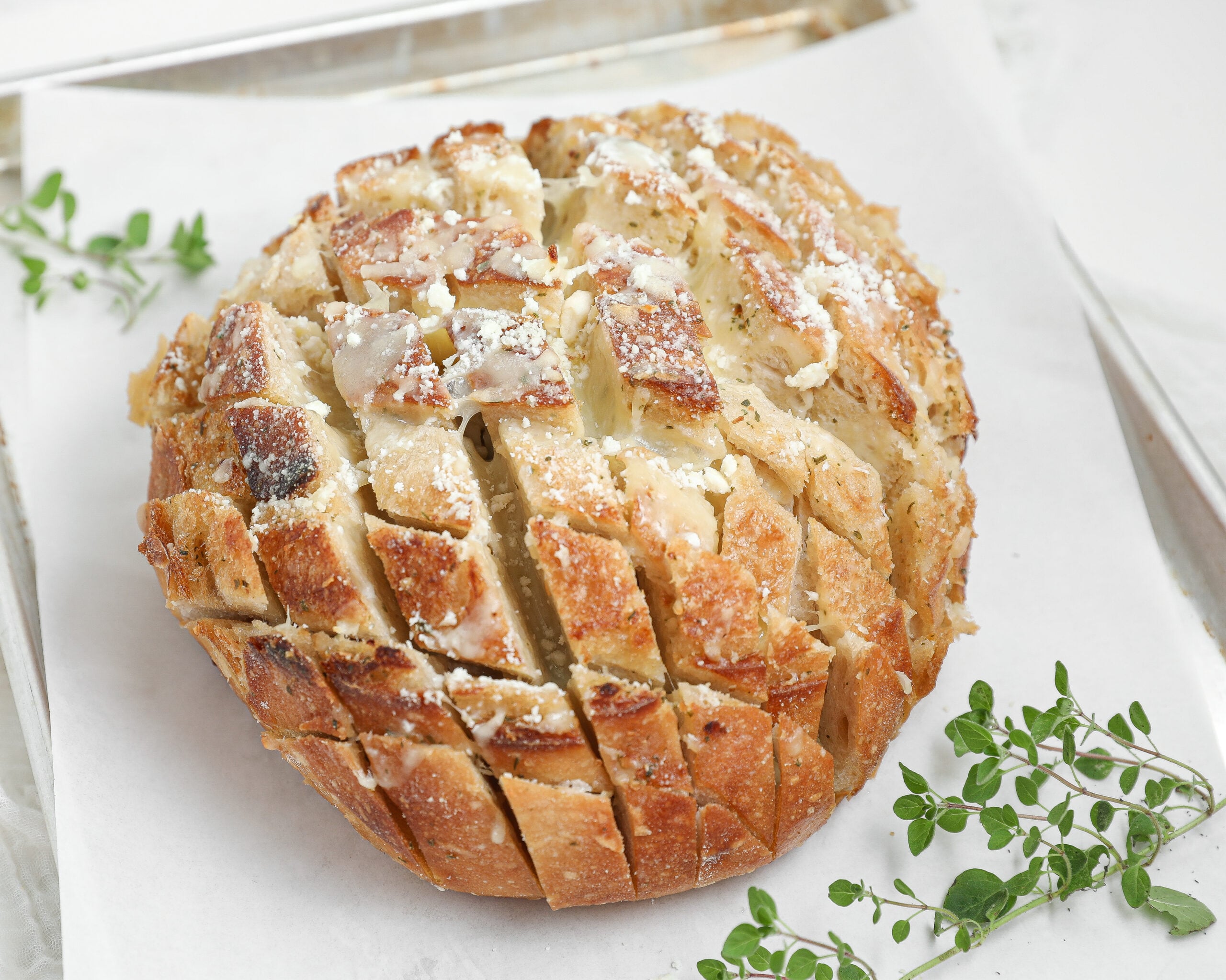 Round loaf of pull apart cheese bread with golden crust, melted mozzarella, Parmesan cheese, and herbs between the slices.