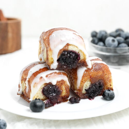 Blueberry pie cinnamon roll bites stuffed with homemade blueberry filling and topped with sweet glaze on a white plate.