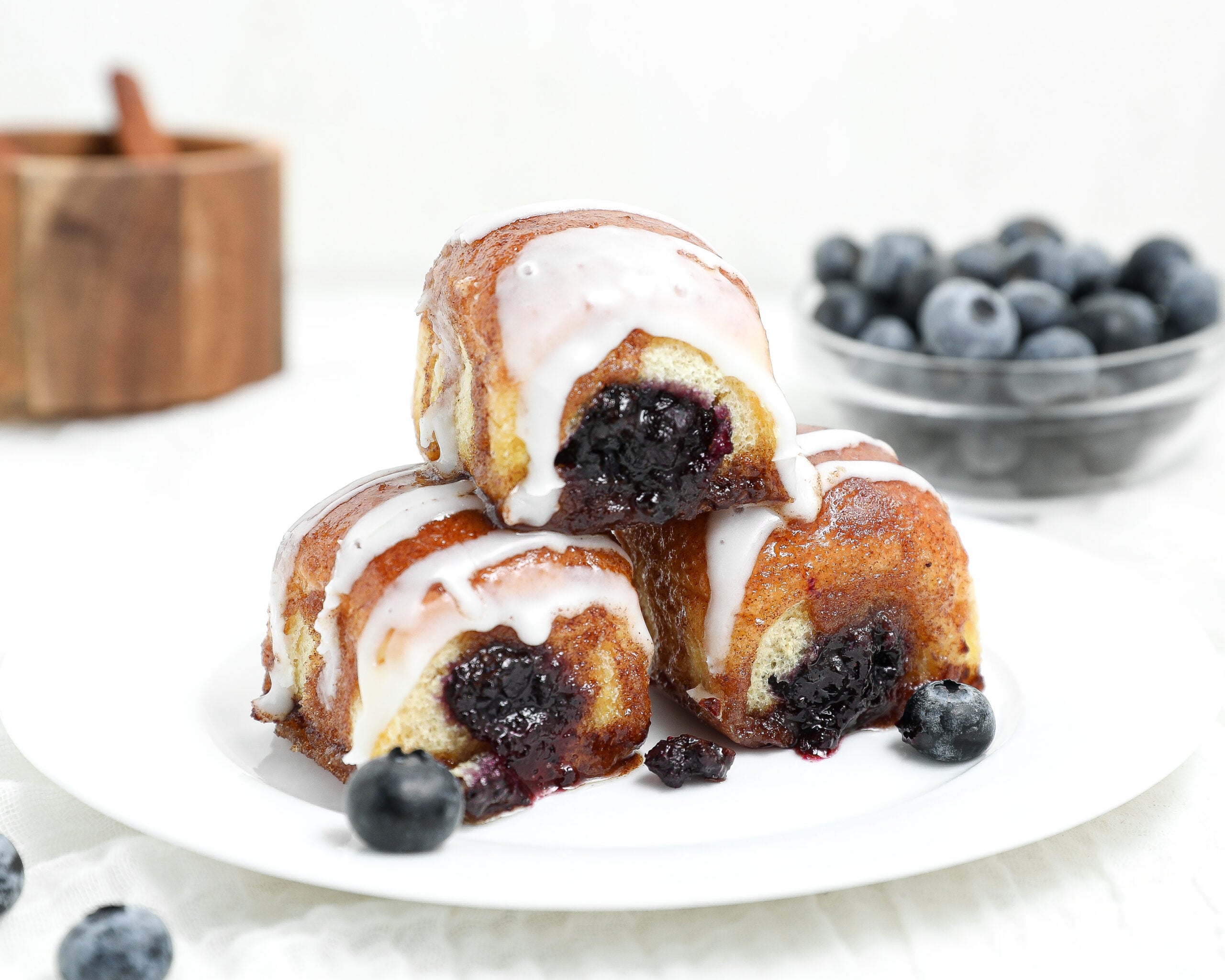 Blueberry pie cinnamon roll bites stuffed with homemade blueberry filling and topped with sweet glaze on a white plate.