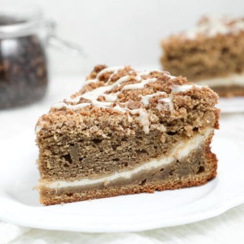 Slice of coffee latte coffee cake with a cream cheese center, espresso crumb topping, and maple glaze on a white plate.