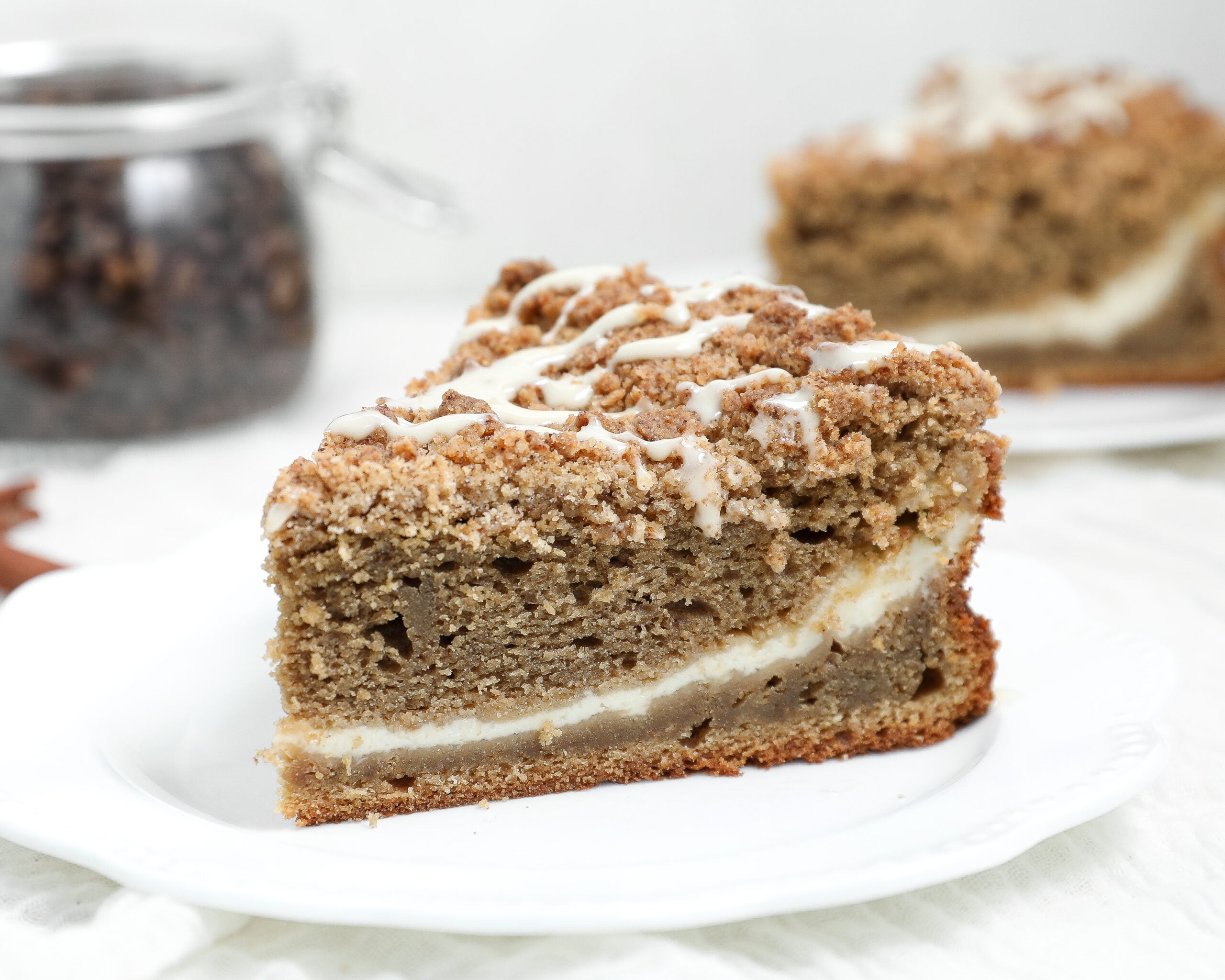 Slice of coffee latte coffee cake with a cream cheese center, espresso crumb topping, and maple glaze on a white plate.