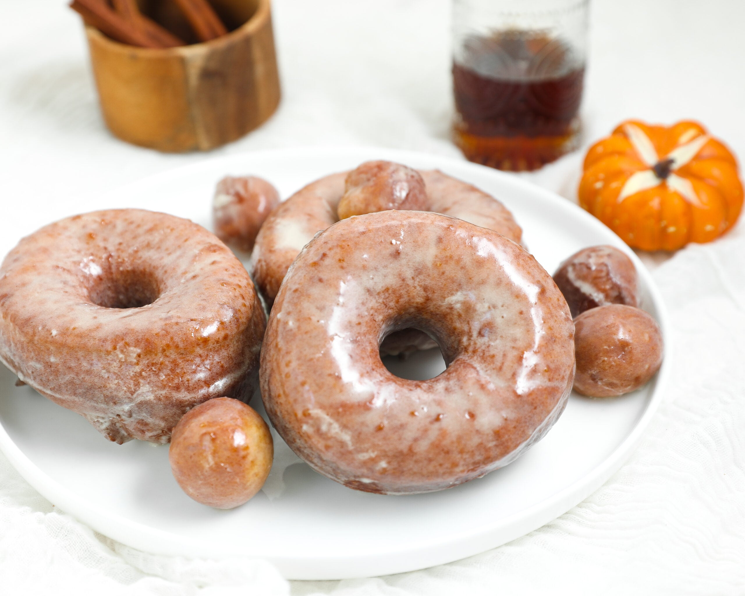 Soft pumpkin doughnuts covered in maple glaze on a white plate with pumpkin doughnut holes and fall decorations.