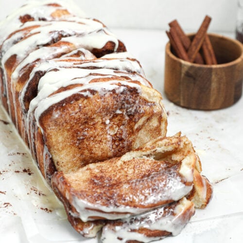 Homemade cinnamon roll pull apart bread with cinnamon sugar layers and cream cheese glaze, with a slice pulled away from the loaf.