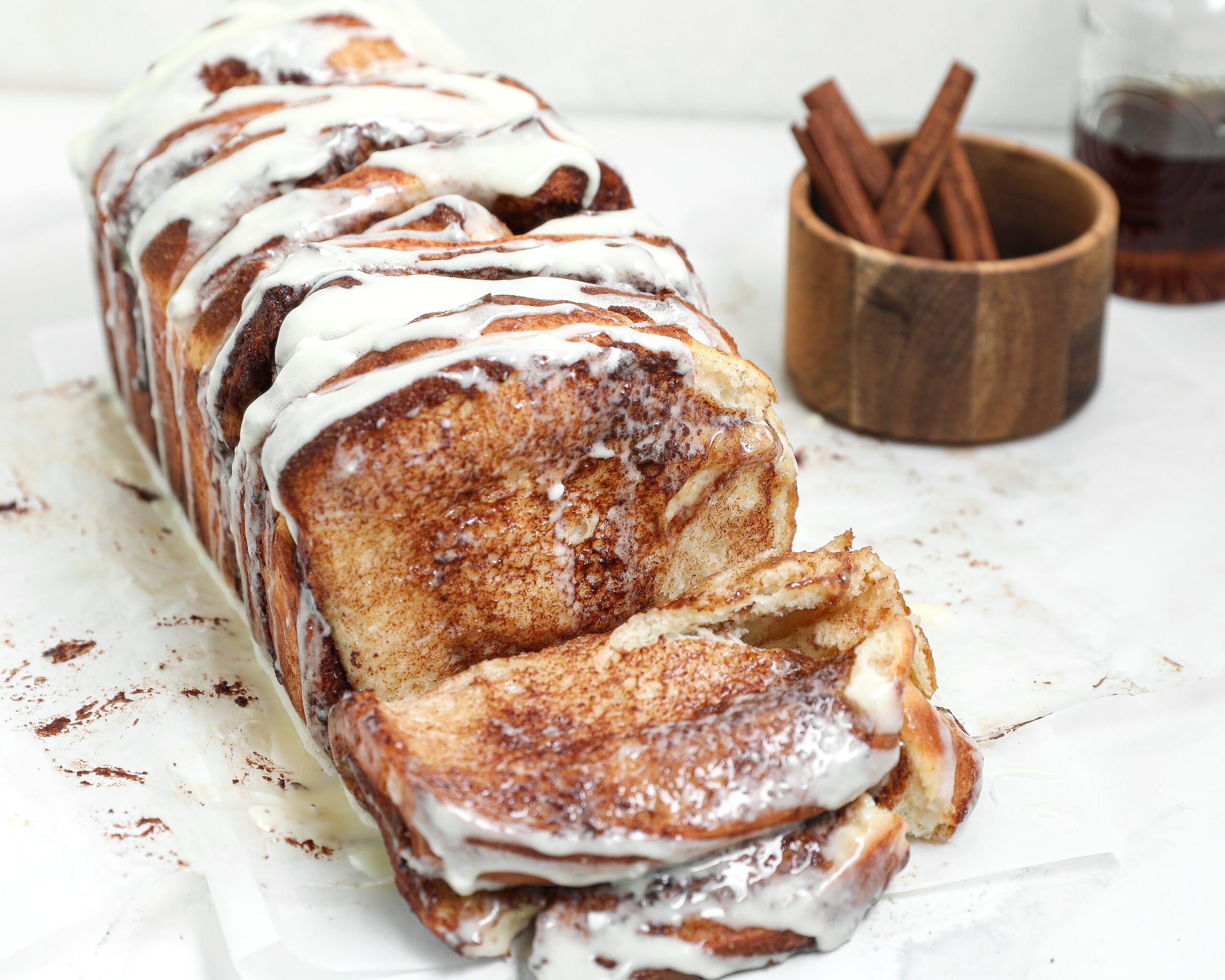 Homemade cinnamon roll pull apart bread with cinnamon sugar layers and cream cheese glaze, with a slice pulled away from the loaf.