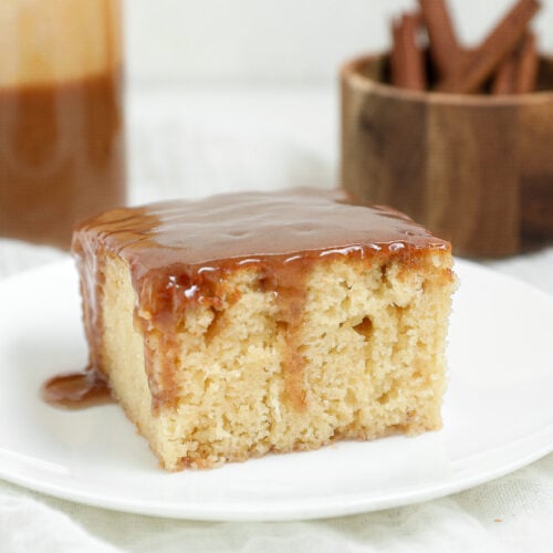 Slice of Sticky Pudding Cinnamon Roll Cake topped with glossy cinnamon toffee sauce on a white plate.