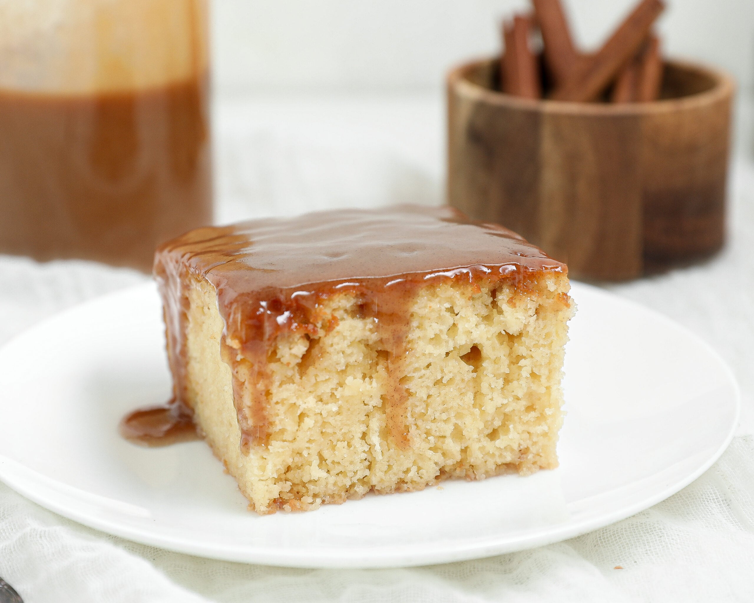 Slice of Sticky Pudding Cinnamon Roll Cake topped with glossy cinnamon toffee sauce on a white plate.