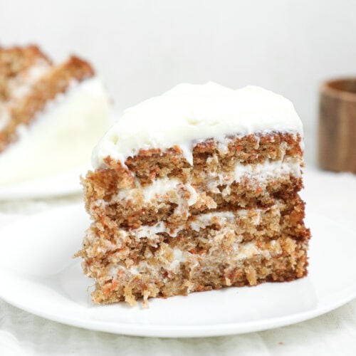 Slice of moist pineapple carrot cake with layers of cream cheese frosting and a thick layer of frosting on top, served on a white plate.