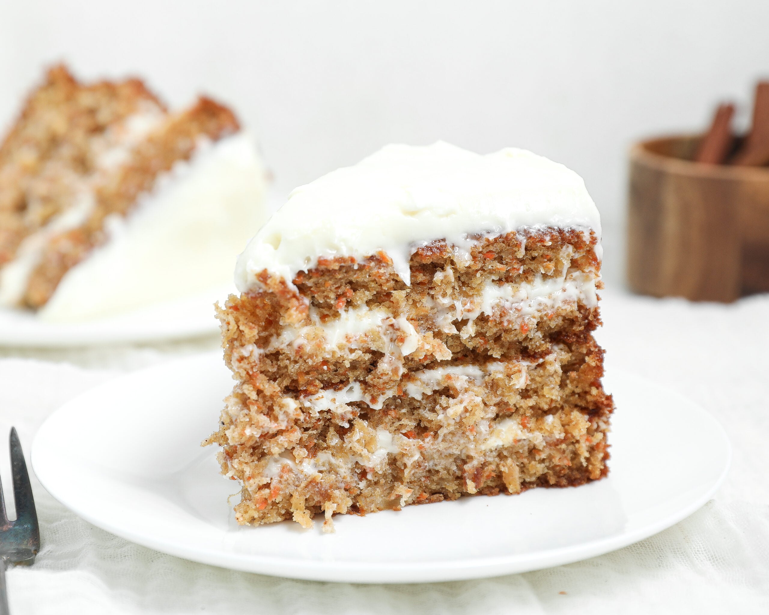 Slice of moist pineapple carrot cake with layers of cream cheese frosting and a thick layer of frosting on top, served on a white plate.