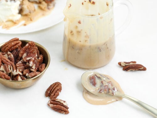 Easy pecan praline sauce with toasted pecans in a small pitcher and spoon