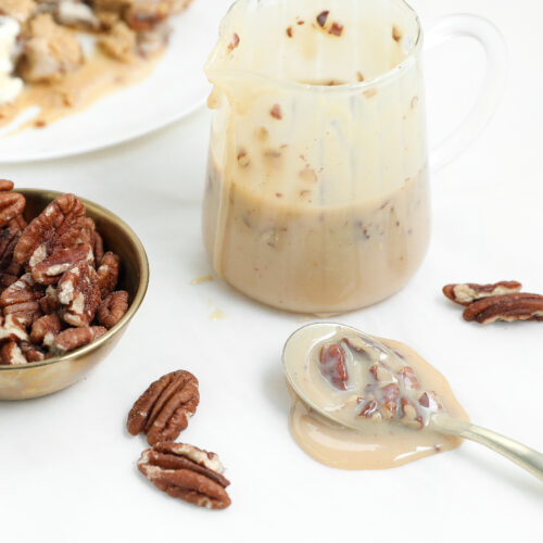 Easy pecan praline sauce with toasted pecans in a small pitcher and spoon