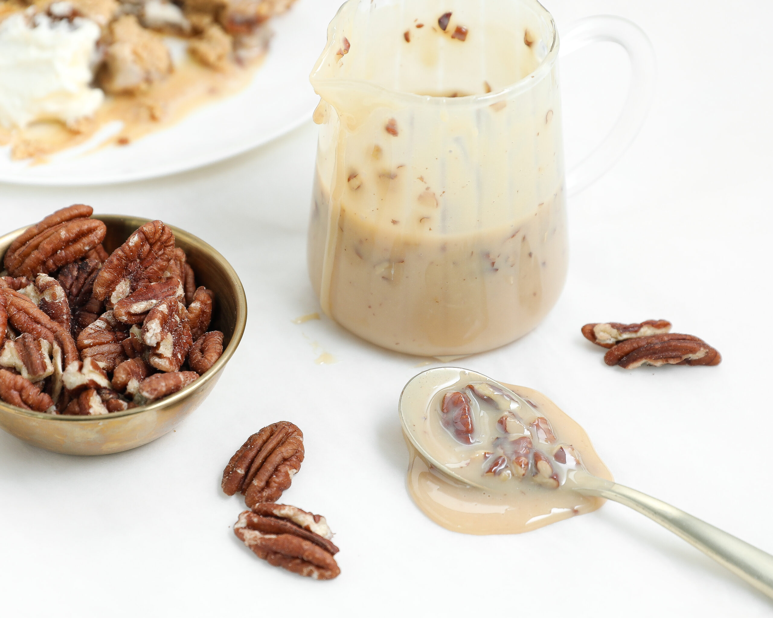Easy pecan praline sauce with toasted pecans in a small pitcher and spoon