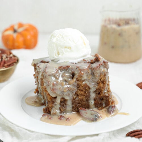 A slice of pecan praline sticky pudding cake covered in creamy pecan sauce and topped with vanilla ice cream on a white plate.